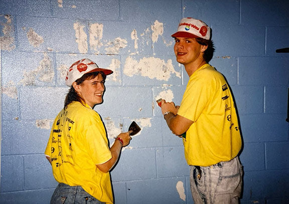 Two volunteers for Week of Caring scape paint off a wall, 1990s