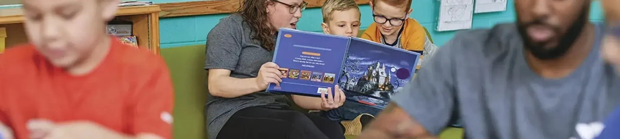 A woman reads to two young children in an activity room at the YMCA