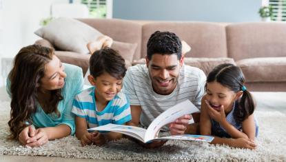 Parents and children lying on rug reading story book together