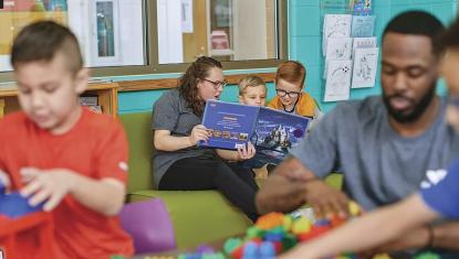 A woman reads to two young children in an activity room at the YMCA